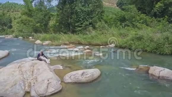 一个家伙在石头上和袋子一起潜入急流中的河流视频的预览图