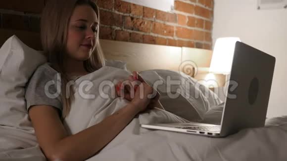 晚上躺在床上女人在笔记本电脑上聊天视频的预览图