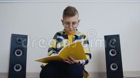 戴着教科书的眼镜的漂亮男孩坐在家里的地板上在那里记录了一些有趣的东西学生视频的预览图