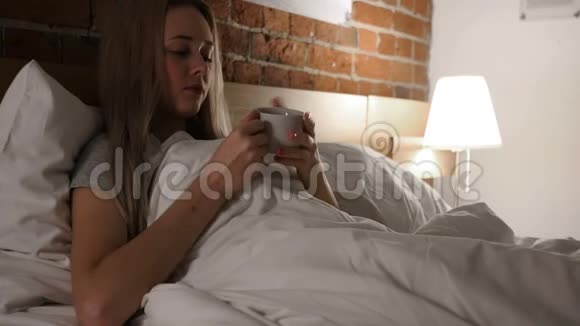 年轻女子晚上在床上喝热咖啡视频的预览图