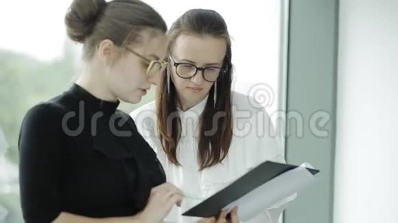 两位年轻的美女在窗户附近讨论不同的文件视频的预览图