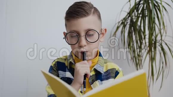 一个戴眼镜的时髦男孩坐在白色墙壁的背景上在笔记本上做有趣的笔记A视频的预览图