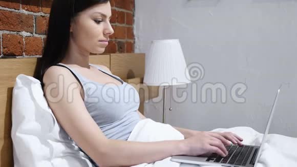 床上兴奋的女人在笔记本电脑上庆祝成功视频的预览图
