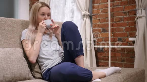 年轻女子喝杯咖啡坐沙发视频的预览图