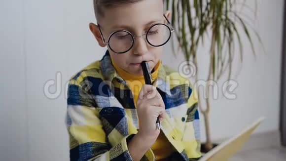 一个戴眼镜的时髦男孩坐在白色墙壁的背景上在笔记本上做有趣的笔记A视频的预览图