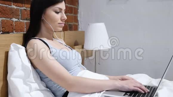 放松的女人在床上玩手机听音乐视频的预览图