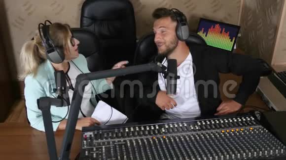 年轻的电台主持人男人和女人在收音机里的声音控制台附近对着麦克风说话视频的预览图