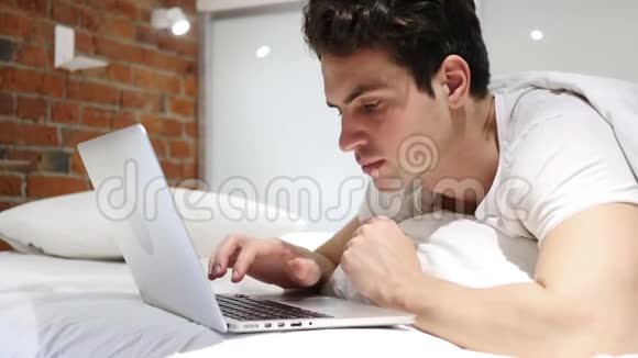 在床上工作的人在笔记本电脑上工作并应对损失失败视频的预览图