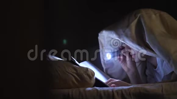 一个孩子晚上用手电筒在毯子下面读一本书热心男孩视频的预览图