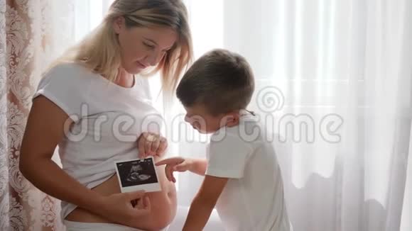 好奇的男孩感兴趣的肚子妈妈抱着超声波扫描的照片视频的预览图