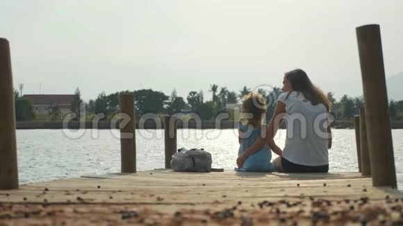 母亲和小女儿坐在码头上慢慢地享受大自然视频的预览图