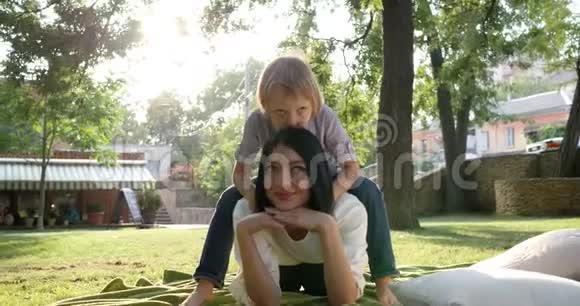 一家人小男孩坐在年轻的母亲面前对着绿色的草地微笑视频的预览图