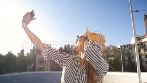 戴帽子戴太阳镜的微笑女人在手机上自拍的慢动作视频视频的预览图