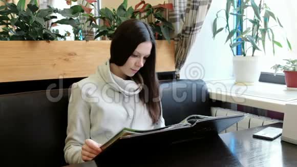 穿着一件轻夹克的布鲁内特年轻女士在咖啡馆里翻阅菜单视频的预览图