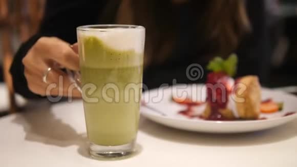 女端着一杯美味的火柴绿茶在咖啡馆4K特写视频的预览图