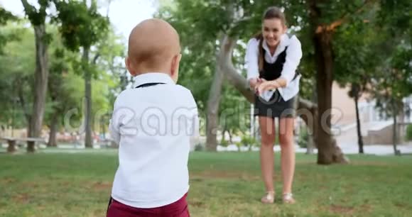 小男孩光着脚在草地上散步背景是年轻母亲在户外视频的预览图