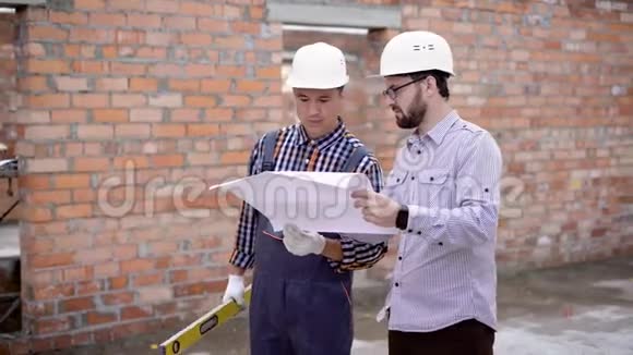一个戴着头盔的工程师和一个长着胡须的成年建筑师考虑一个施工图其中的方案为视频的预览图