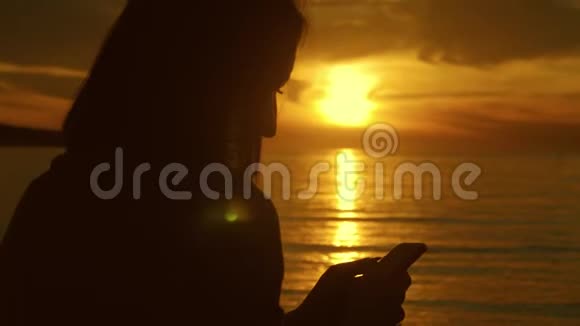 年轻女游客在海洋海滩日落时使用电话剪影一直连接互联网的概念视频的预览图