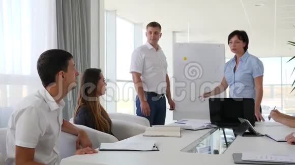 伙伴们坐在桌子上在白色宽敞的办公室里开会听两个人讲话视频的预览图