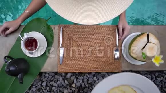高角度拍摄戴大帽子的女孩在游泳池里吃早餐异国风味的民族菜肴视频的预览图