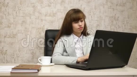 漂亮的女孩坐在办公室的椅子上在笔记本电脑上打字喝着白色杯子里的咖啡年轻女子视频的预览图