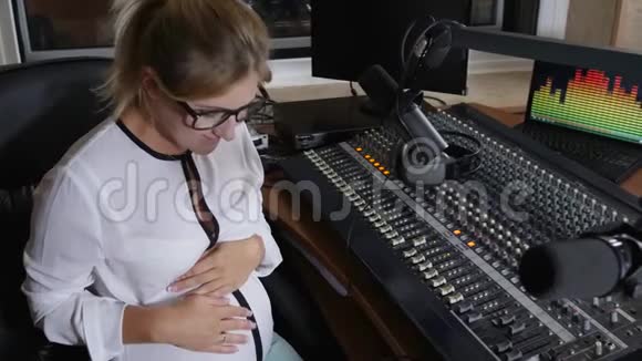 现代妈妈在广播演播室抱着爱抚大肚子有害工作视频的预览图
