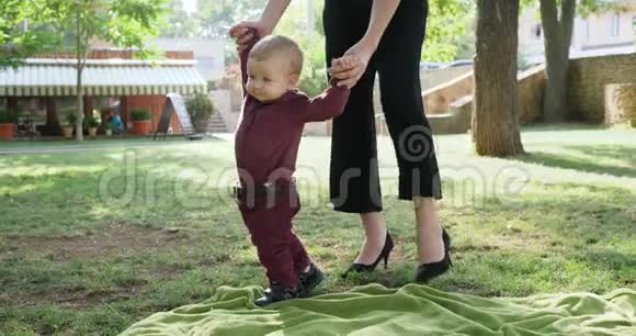 妈妈帮助儿子在户外迈出第一步妈妈支持她的小宝宝练习他的第一步视频的预览图