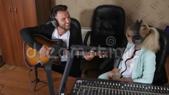 耳机里的快乐女人采访在演播室弹吉他的男人视频的预览图