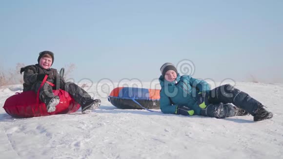 两个孩子骑在雪橇上的雪山上孩子们坐在山顶上体育和户外活动视频的预览图