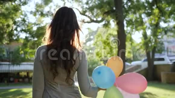 年轻女子穿着衣服背着五颜六色的气球在公园里微笑快乐的情绪视频的预览图