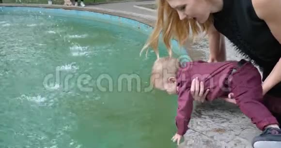 幸运的是婴儿试图缓慢地触摸喷泉中的水母亲抱着她的儿子靠近水视频的预览图
