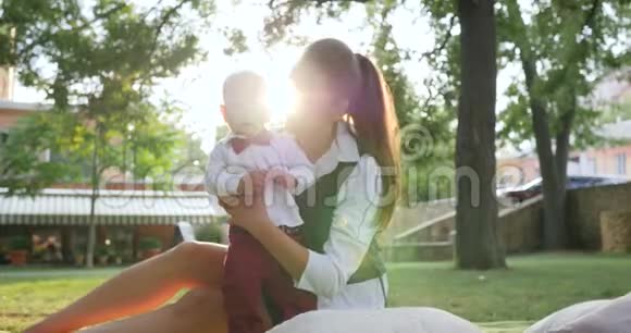 穿着西装领结的漂亮男孩靠在妈妈身边坐在绿色草坪上视频的预览图