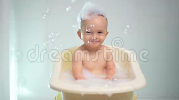 可爱的小男孩坐在浴缸里看五颜六色的肥皂泡的慢动作视频视频的预览图