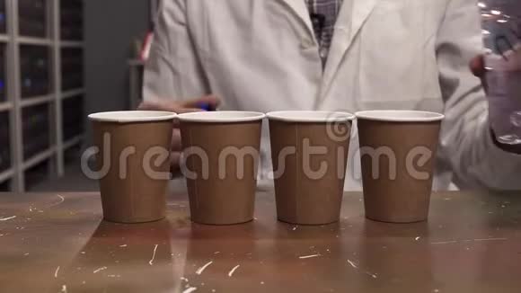 穿着白色实验服的人把水从塑料瓶倒入四个纸杯视频的预览图