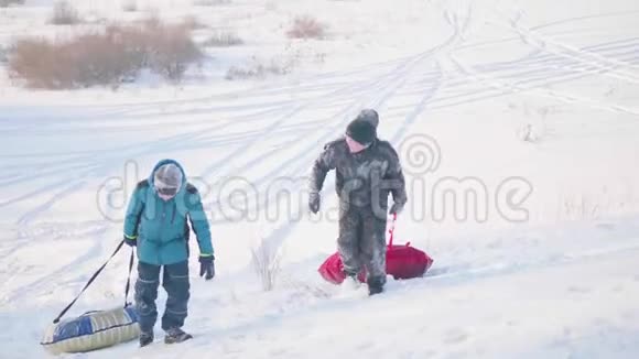 两个孩子骑在雪橇上的雪山上孩子们爬到山顶在新鲜空气中游走视频的预览图