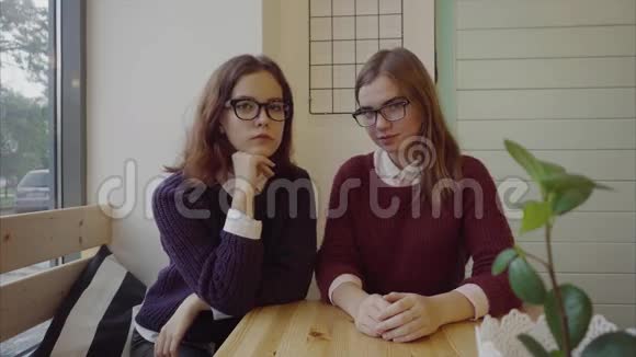 两个漂亮的女生戴着眼镜坐在咖啡馆的桌子旁看着镜头视频的预览图