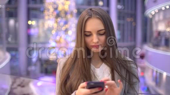 年轻女性在模糊的大商场背景下使用现代智能手机浏览互联网或短信4k视频的预览图