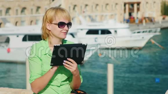 一位女游客在海湾和游艇的背景下享受这款平板电脑视频的预览图