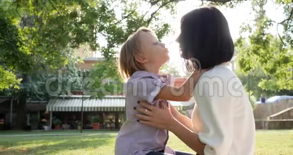 年轻的母亲在公园的背光处亲吻儿子的嘴唇视频的预览图