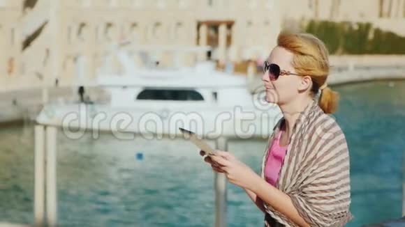 一位女游客在海湾和游艇的背景下享受这款平板电脑视频的预览图