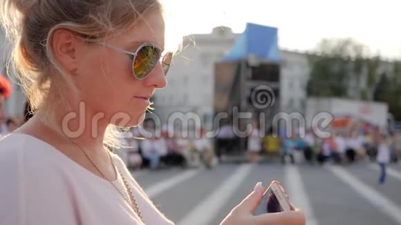戴眼镜的金发女人在市中心的特写镜头中在露天看电话视频的预览图