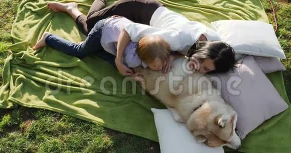 妈妈和儿子拥抱狗躺在公园的绿草上以大自然为背景视频的预览图