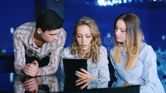 三个朋友一个年轻人和两个女人饶有兴致地看着平板电脑屏幕在咖啡馆里靠在桌子上视频的预览图