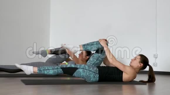 在体育运动中普拉提运动躺在体育垫上两个女孩仰卧交替地拉着膝盖视频的预览图