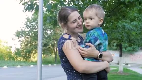 一个快乐的微笑女人在公园拥抱她2岁蹒跚学步的儿子的慢动作视频视频的预览图