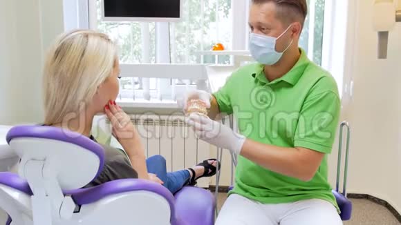 牙科医生给病人展示塑料牙齿模型的4k镜头视频的预览图
