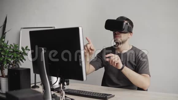 年轻人戴着虚拟现实护目镜坐在办公室里对着电脑试图触摸物体视频的预览图