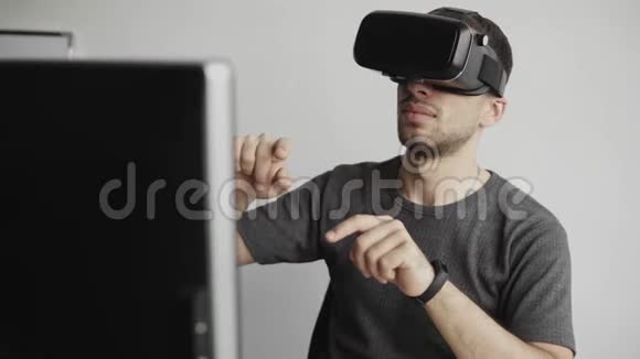 年轻人戴着虚拟现实护目镜坐在办公室里对着电脑试图触摸物体视频的预览图