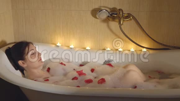 美丽的女人在烛光下沐浴沐浴着泡沫和玫瑰花瓣视频的预览图