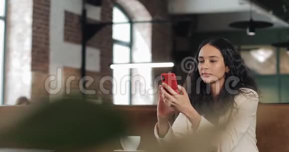 商务女性在智能手机上使用应用程序坐在现代办公室穿着粉色西装的漂亮休闲女性视频的预览图